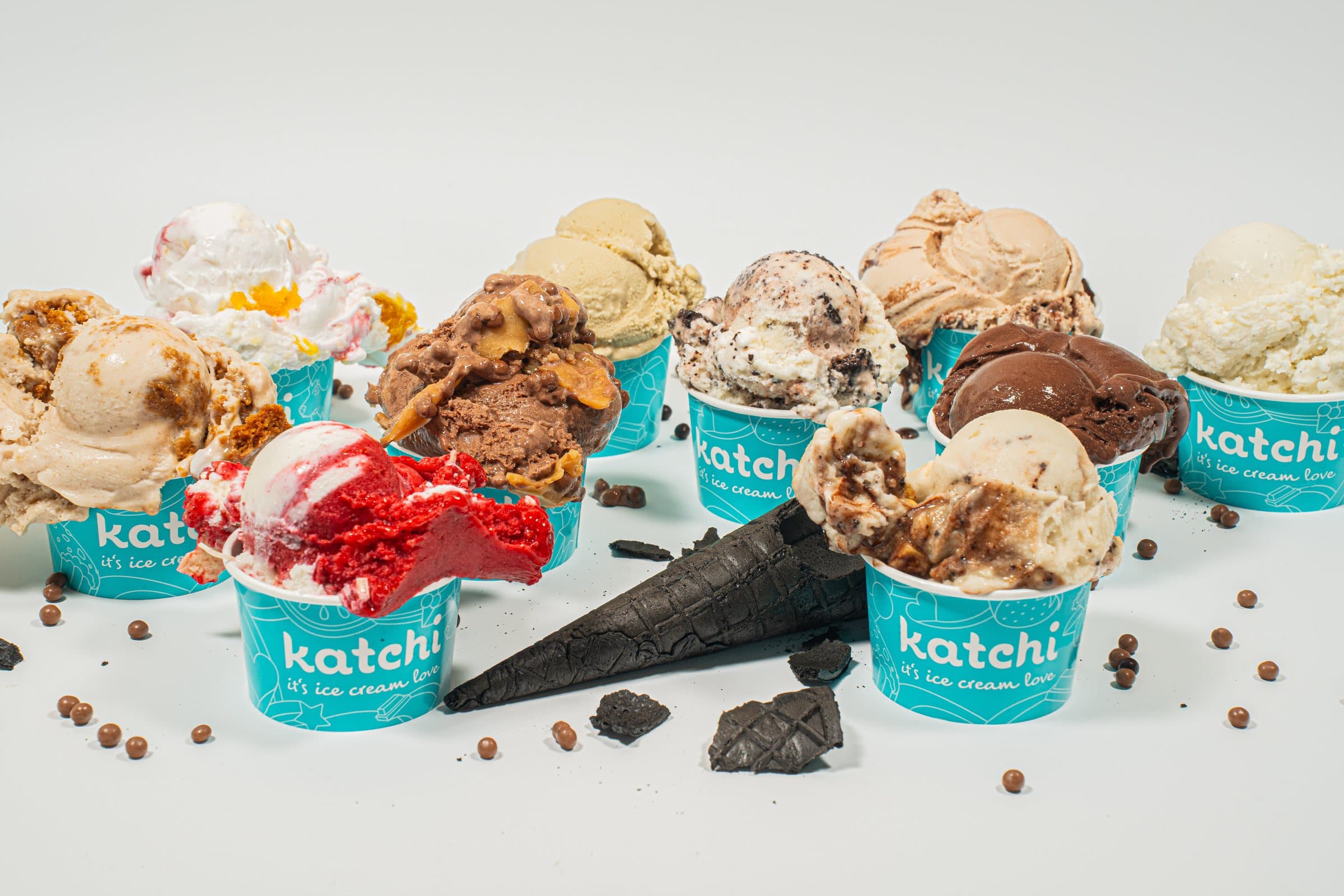 Viele Katchi-Becher mit verschiedenen Eissorten, dazwischen eine schwarze Waffel und Schokoperlen